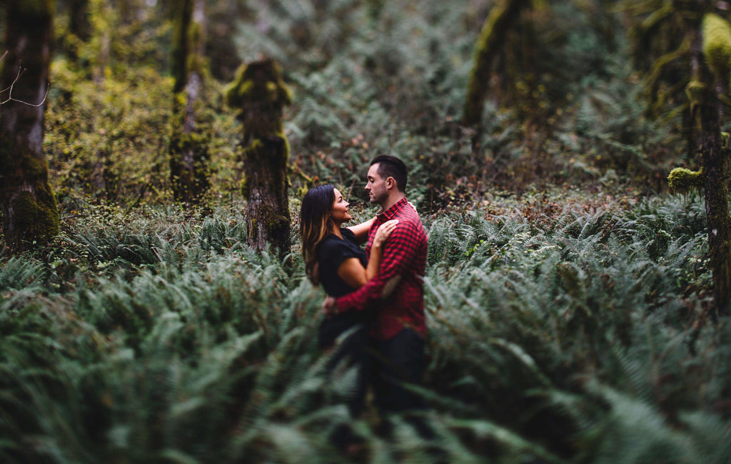 An engagement photo with the couple surrounded by ferns in the woods in Welches, OR