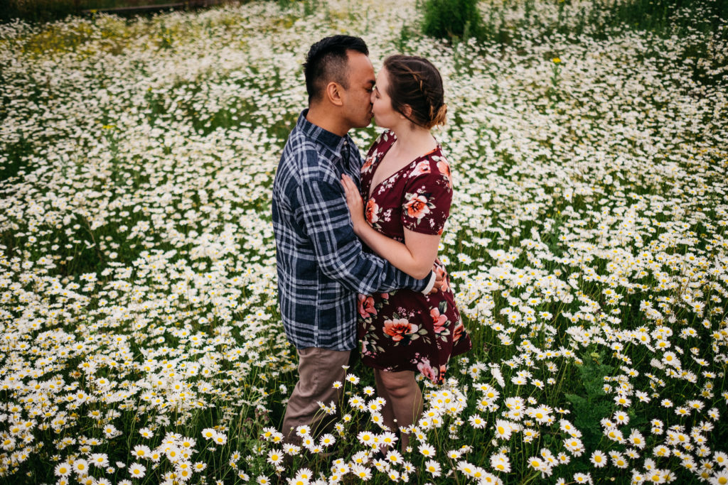 Engagement photo of a couple kissing at Powell Butte in a field of daisies