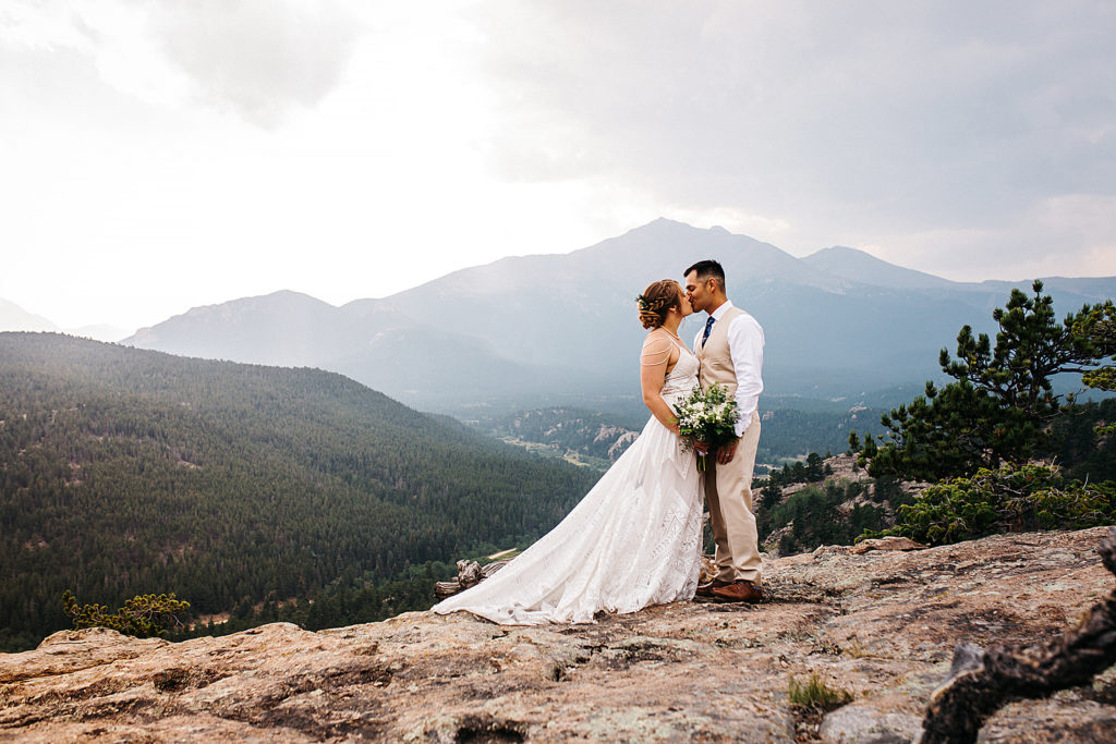 A bride and groom kissing after their elopement in Rocky Mountain National Park with a view of the Rocky Mountains