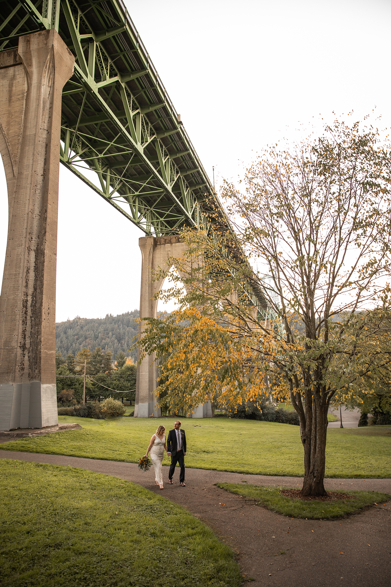 A bride and groom walking beneath the St. John's Bridge in Portland