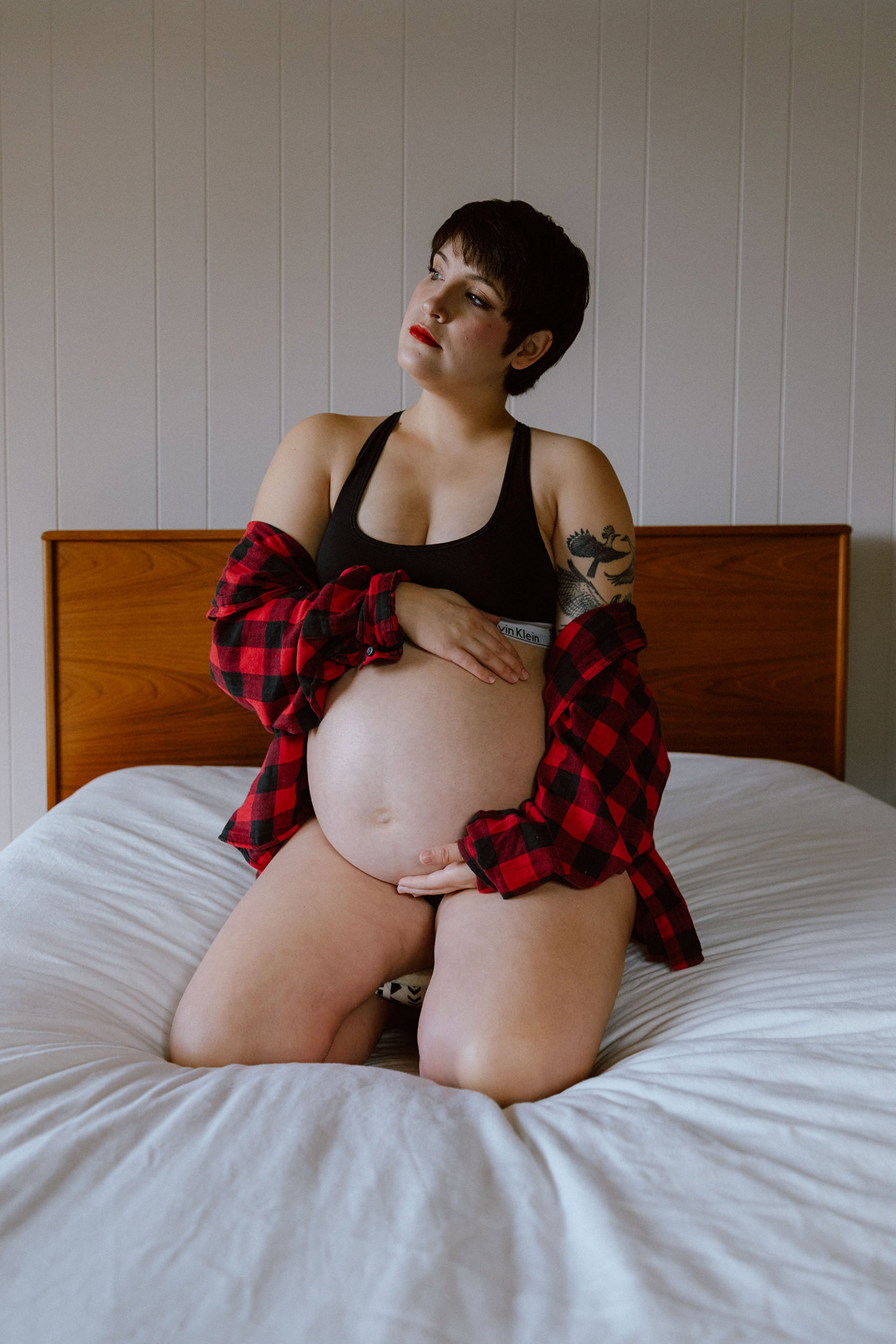 A moody boudoir maternity photo on a bed with natural light