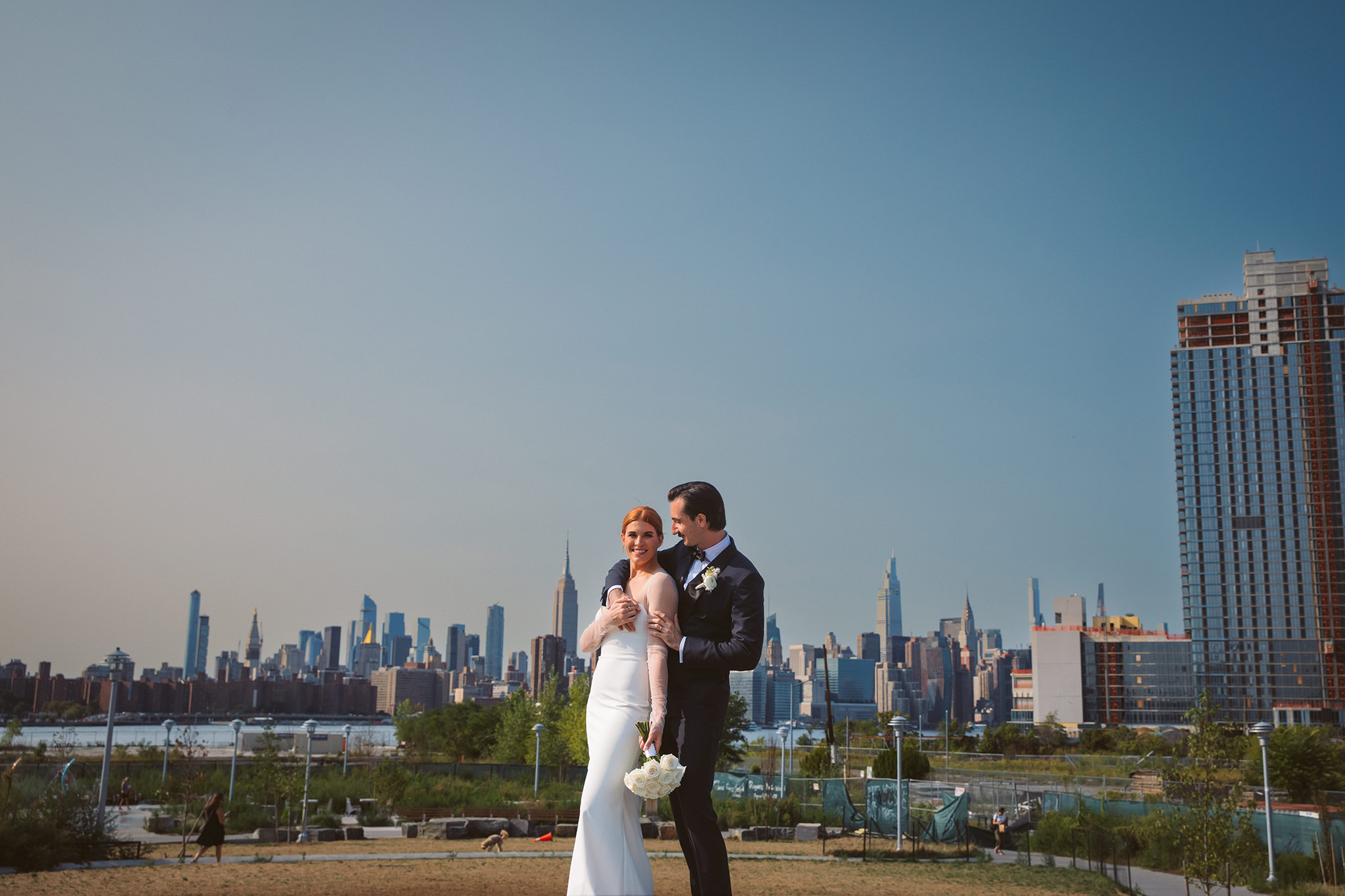 A sunny wedding portrait of a bride and groom with the New York City skyline in the background