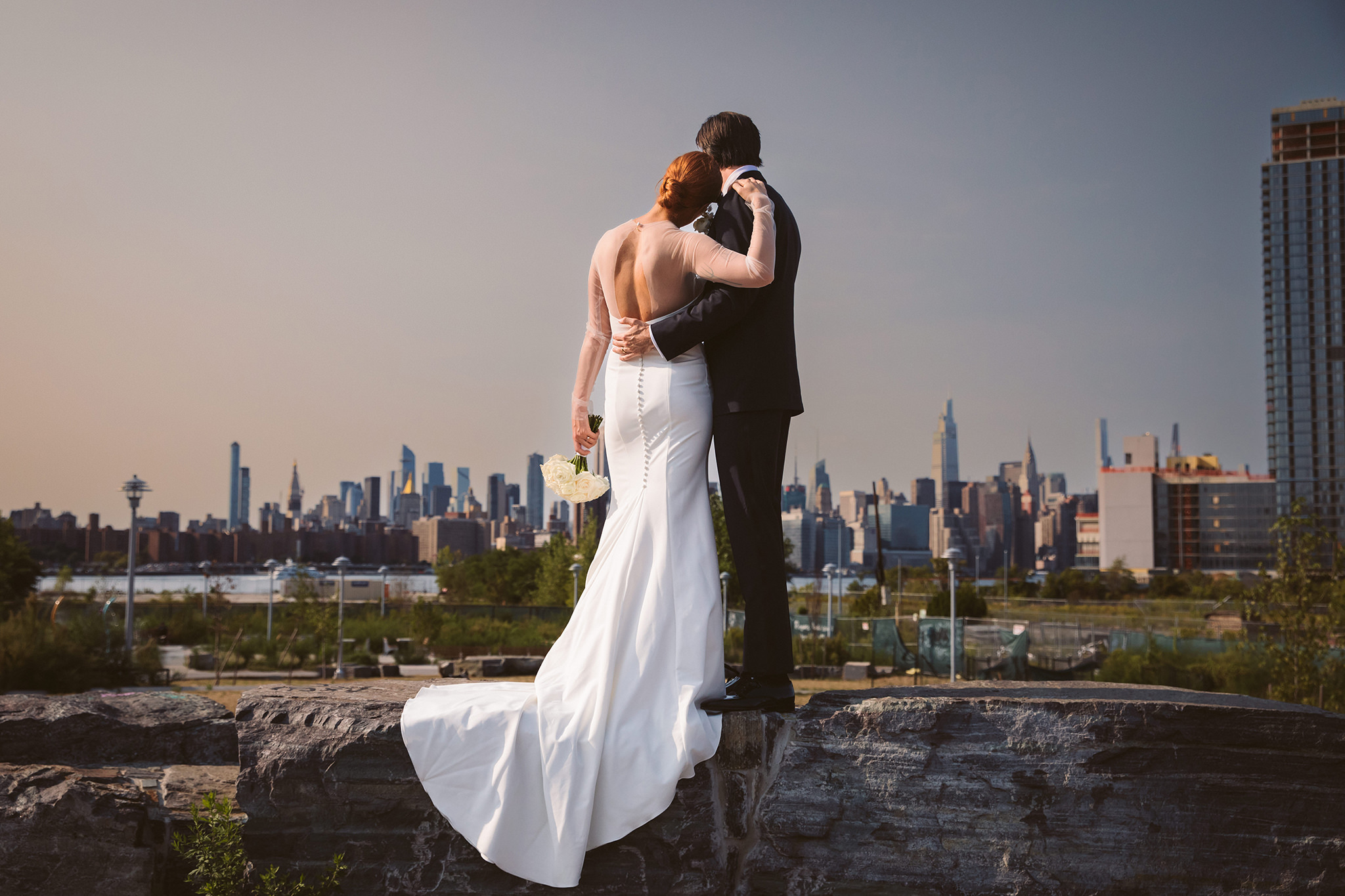 A wedding photo of a bride and groom looking at the Manhattan skyline from Brooklyn in New York