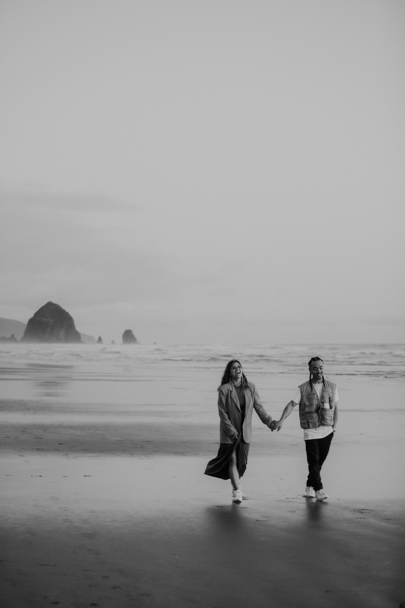 A black and white image of a couple walking along Cannon Beach