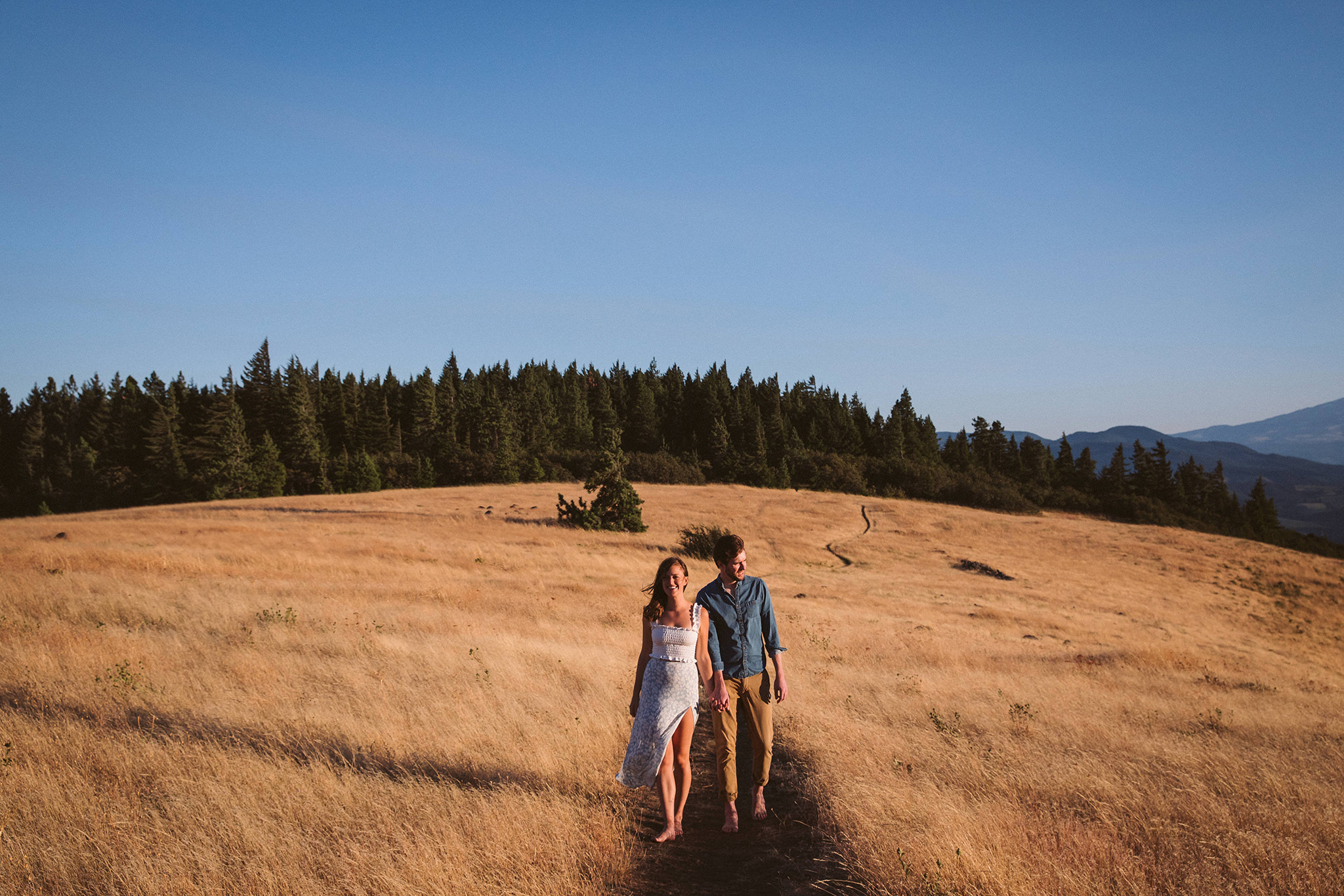 A couple walking in a sunny field of wheat at their Hood River engagement session