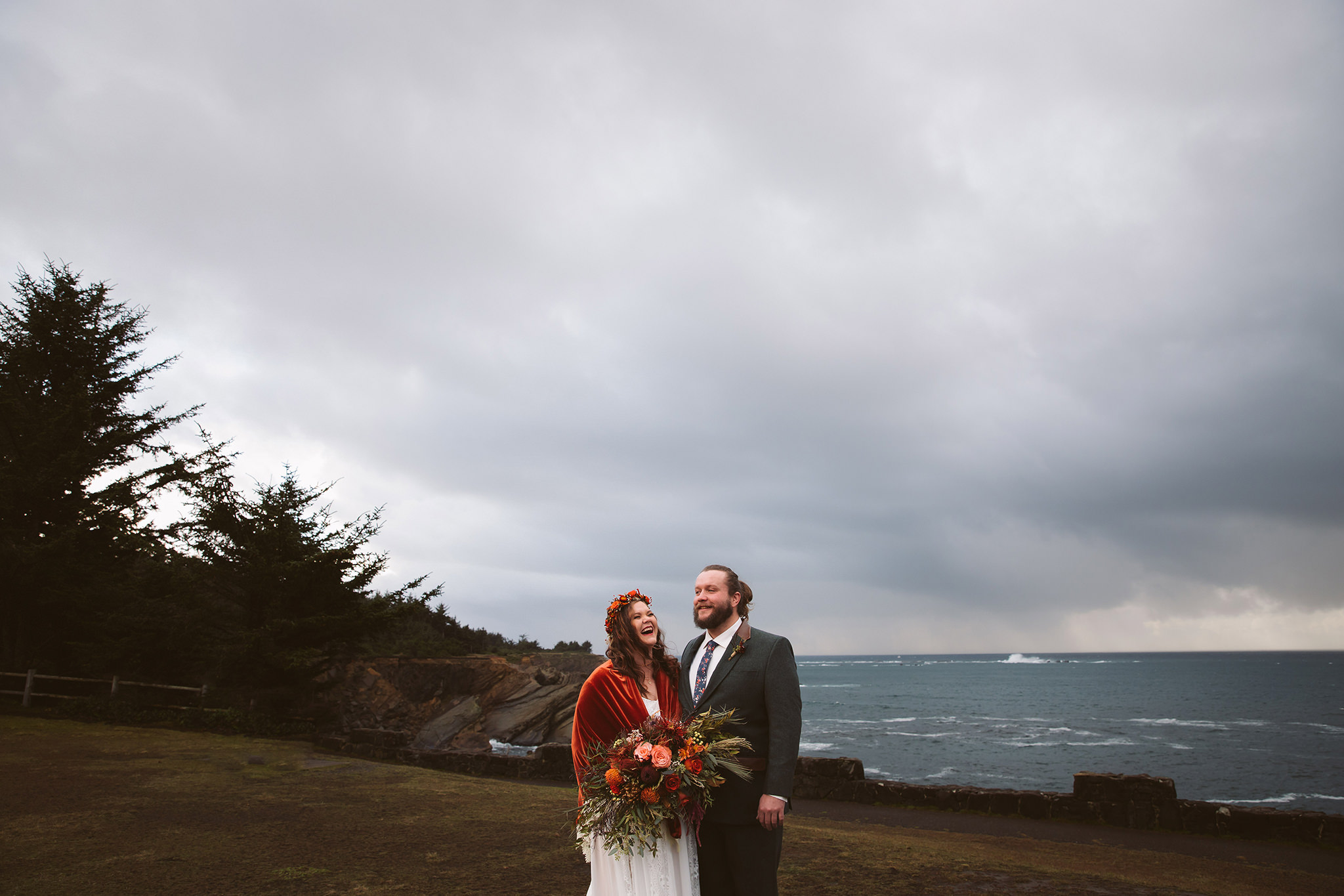 A cinematic wedding photo of a bride and groom with dark cloudy skies and the ocean in the background