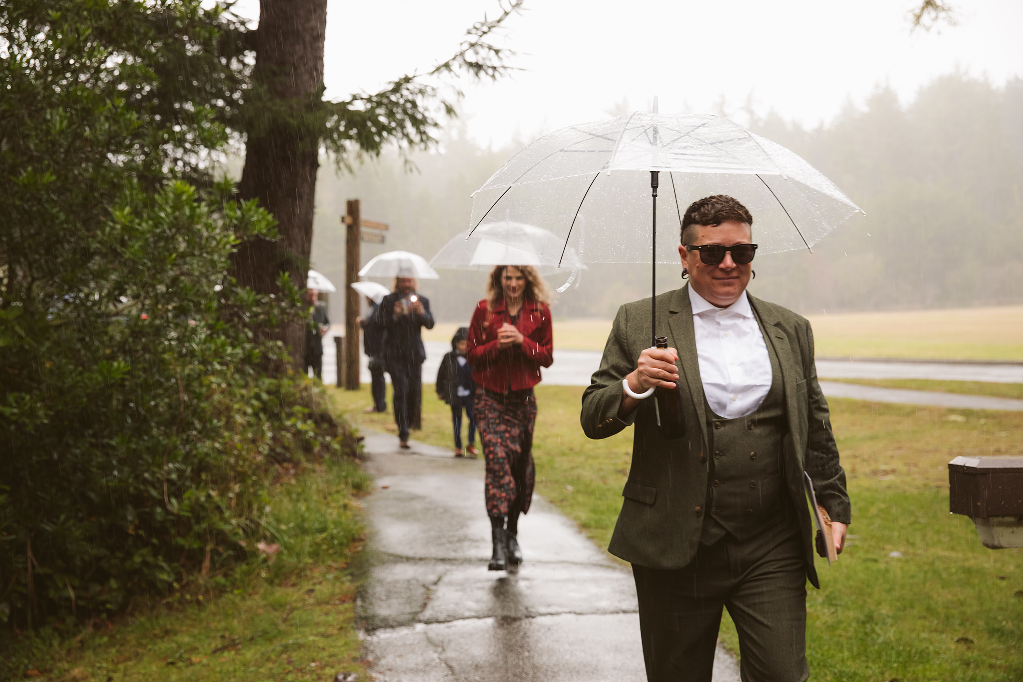 Wedding guests walking with umbrellas in the rain at a shore acres state park elopement