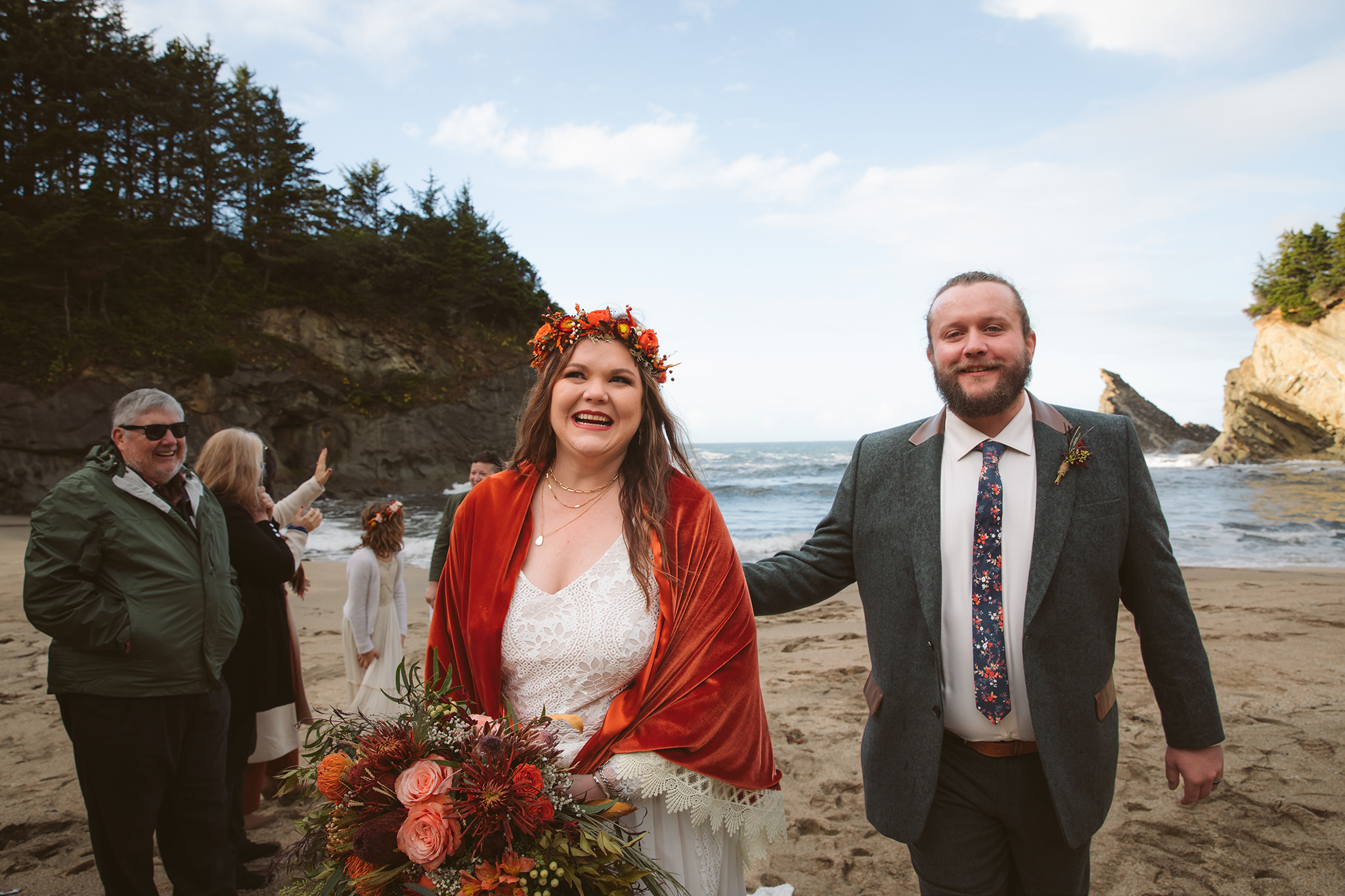 A bride and groom walking together with the ocean in the background after their Oregon coast wedding ceremony