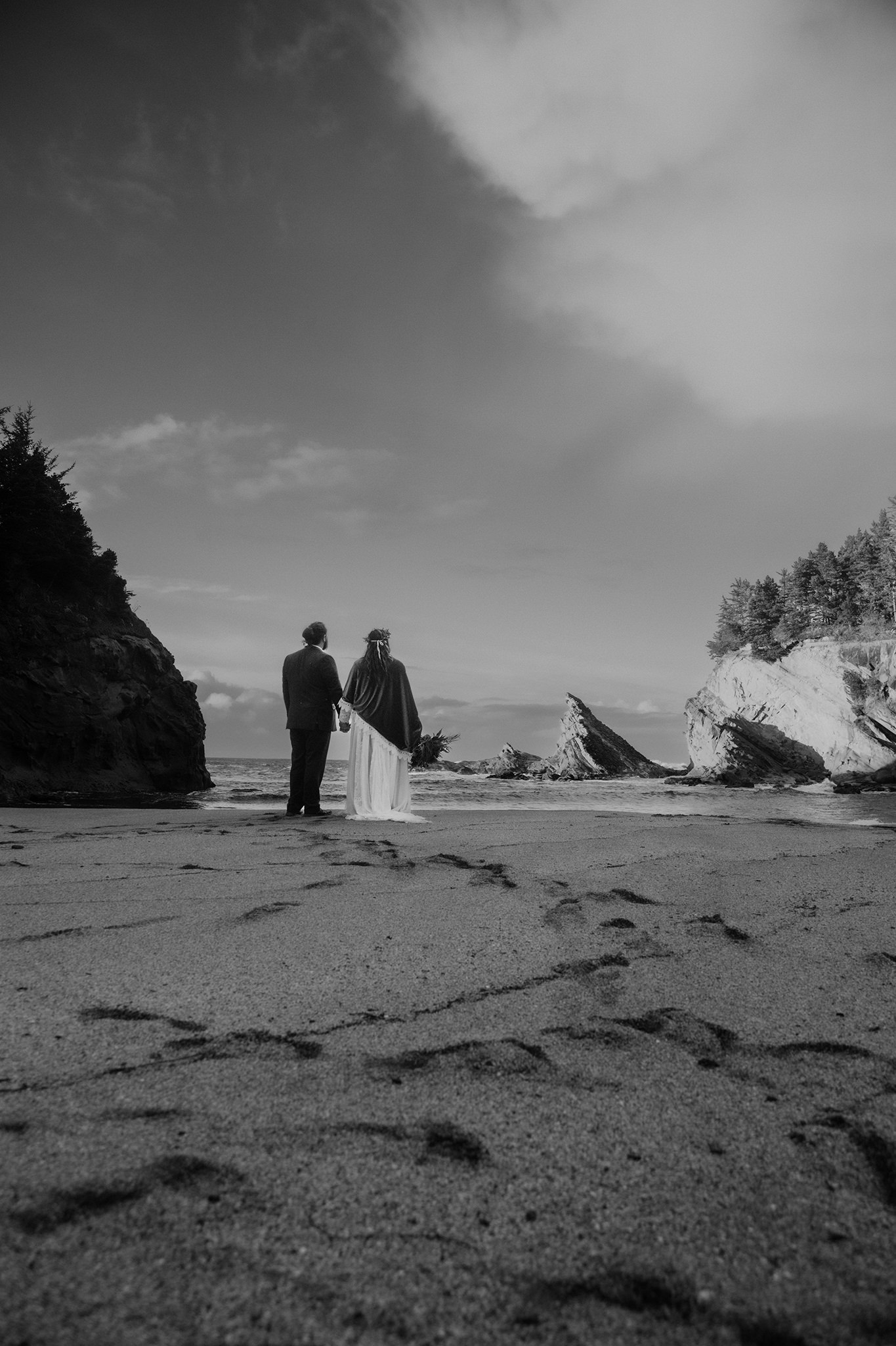 a moody black and white photo of a bride and groom looking out to the ocean on the Oregon coast after their Shore Acres state park wedding