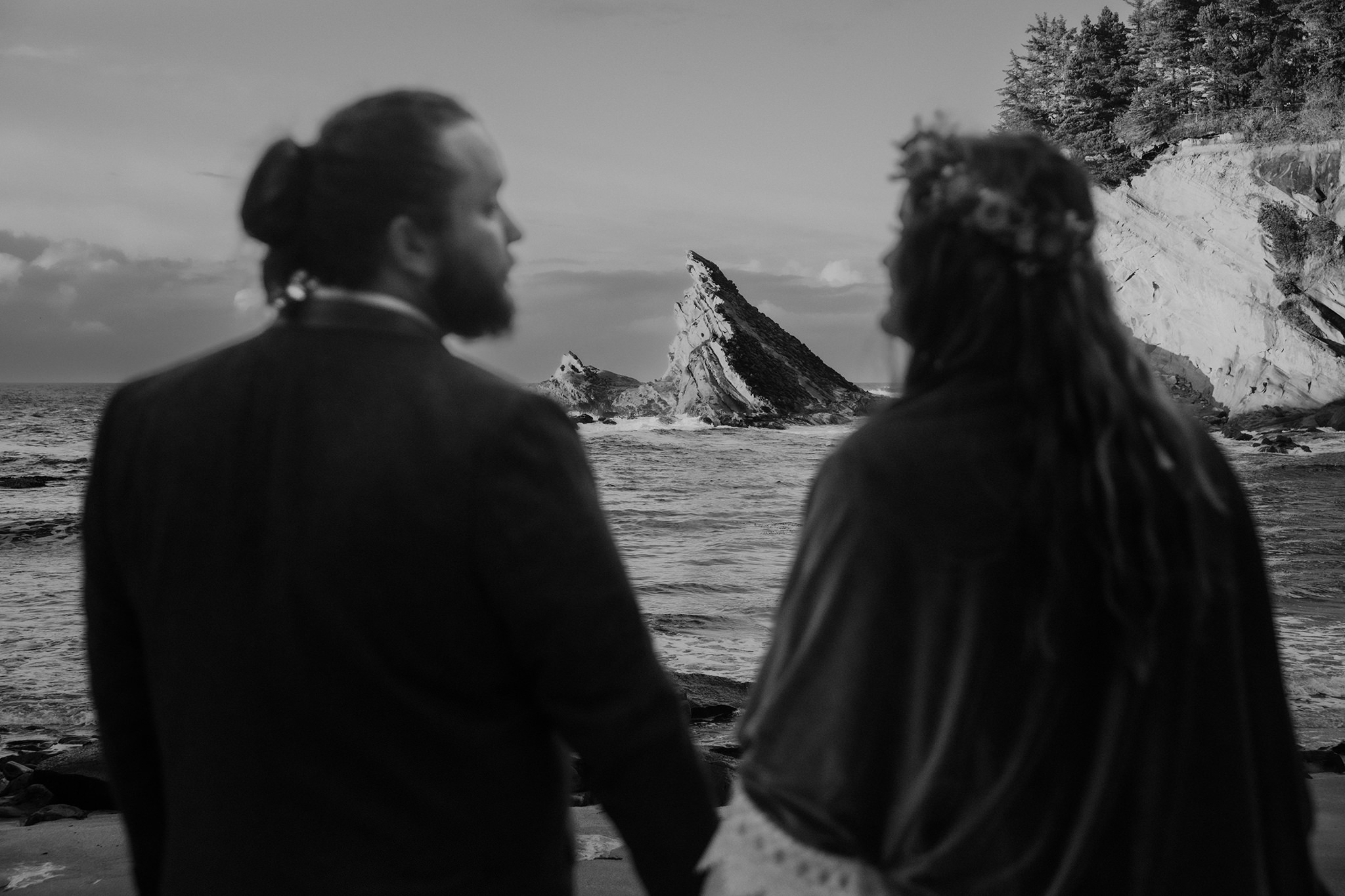 A moody wedding photo of a bride and groom with the jagged Oregon coastline in the background