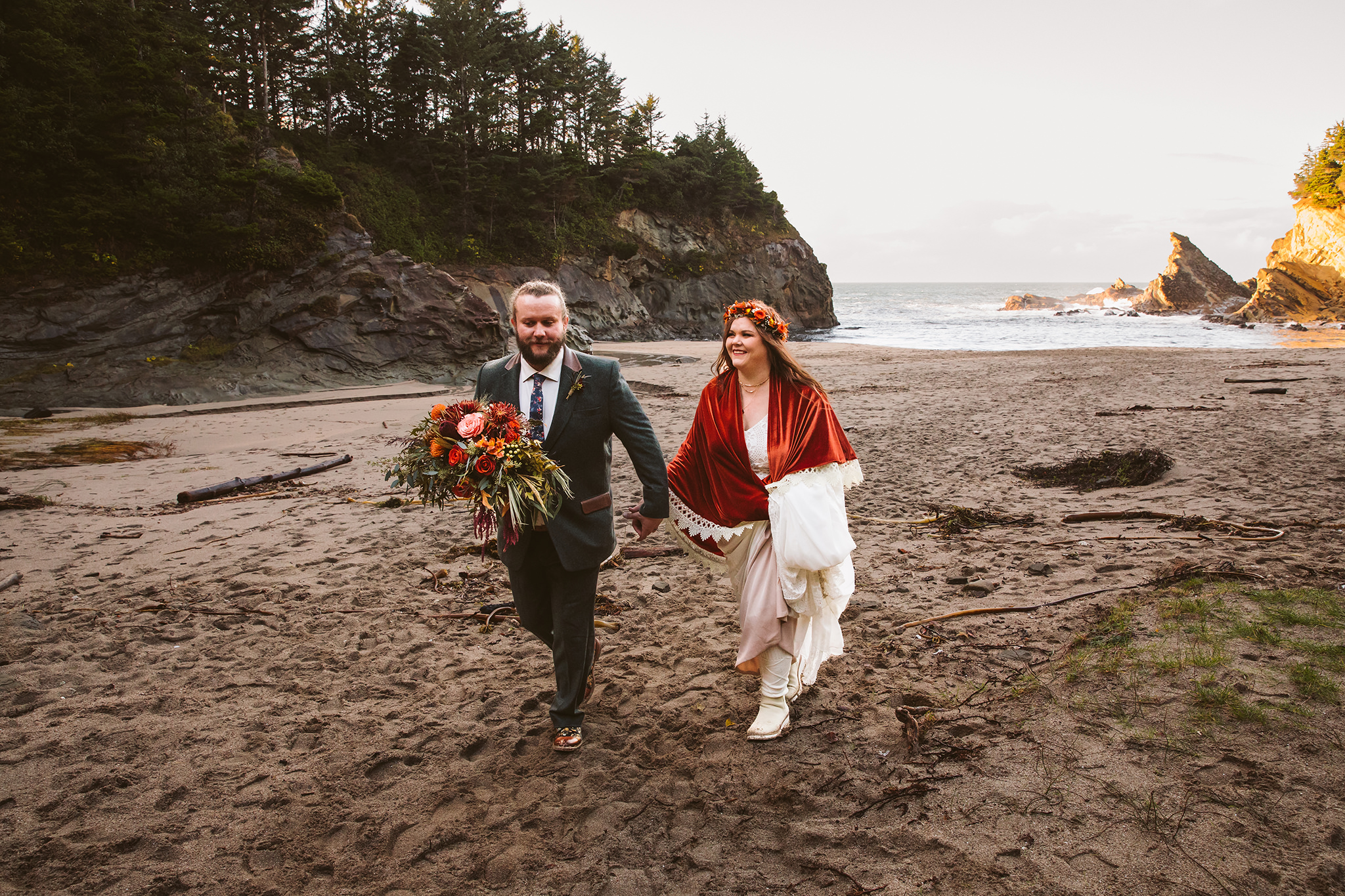 A fall wedding photo of a bride and groom walking on the beach at Shore Acres state park